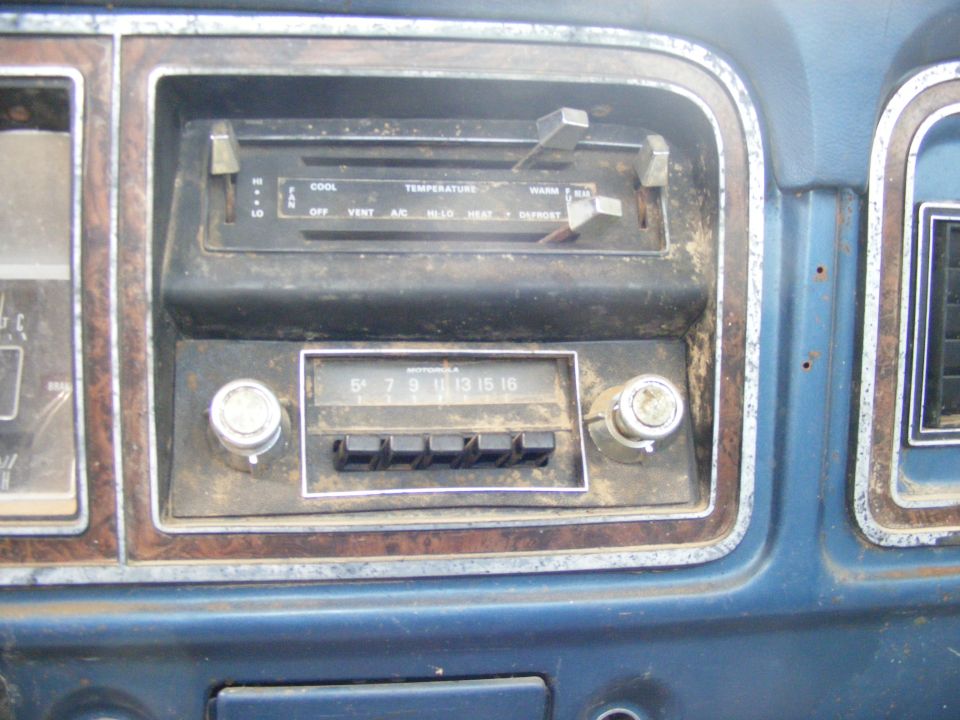 Close-up of a dusty vintage car dashboard with a Motorola radio and climate controls.