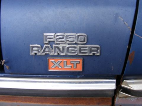 1985 Ford Bronco - The rear of a blue Ford truck is shown with chrome badging that reads "F250 RANGER XLT". The vehicle shows signs of rust and wear.