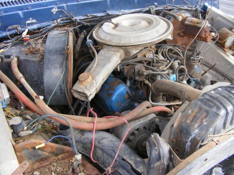 1985 Ford Bronco - The engine bay of a blue Ford Bronco is shown, filled with various engine components, hoses, and wiring. The engine appears to be older and…