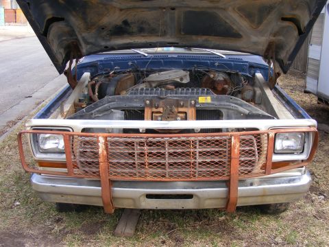 1985 Ford Bronco - The front view of a blue Ford Bronco with its hood open, revealing the engine bay. A rusted metal grille guard is attached to the front bum…