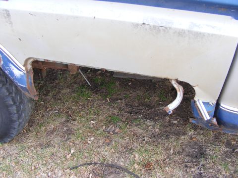 1985 Ford Bronco - Close-up view of the lower rear quarter panel and wheel well area of a vintage vehicle, showing significant rust and damage. A portion of t…