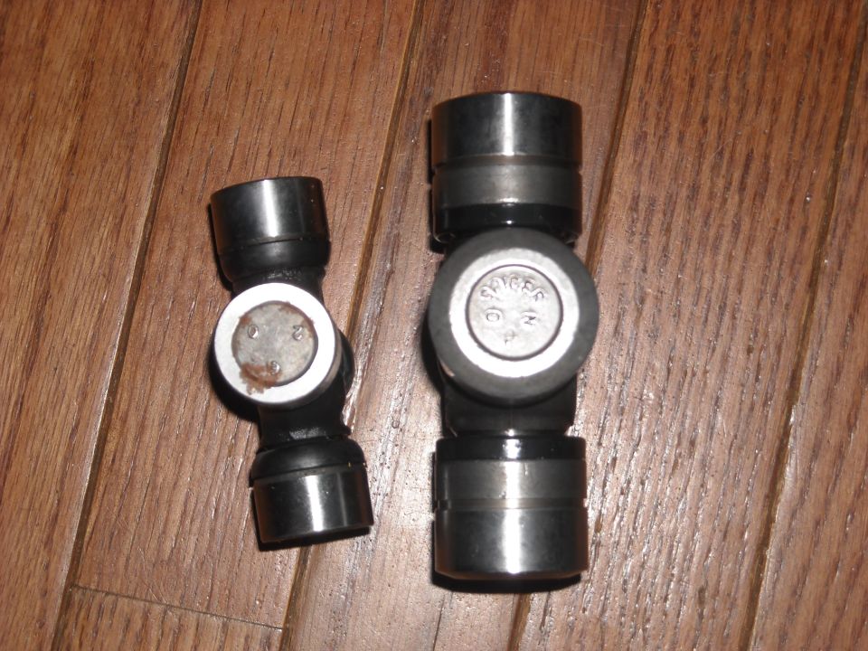 Photo of a partially disassembled universal joint with separated bearing caps on a wood floor.