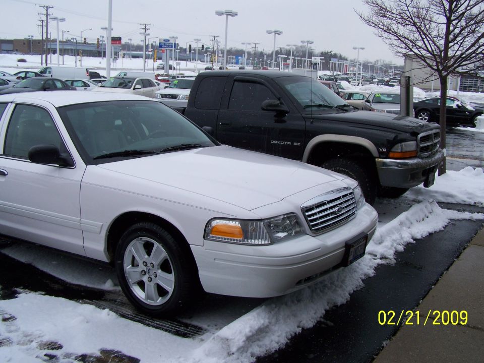 White 2008 Ford Crown Victoria parked next to a black Dodge Dakota pickup truck in a snowy lot.