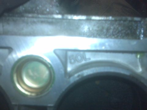 1995 Ford Bronco - A close-up view of a metal engine component with the text "60L" cast into it. A circular opening with a green-tinted insert is visible on t…