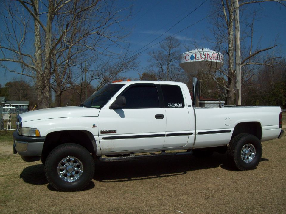 White lifted Dodge Ram pickup truck with chrome wheels and large exhaust pipe.