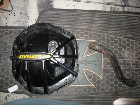 1987 Ford Bronco - A black Dynatrac differential cover is shown with a bent metal piece resting on a textured mat with a cross emblem.