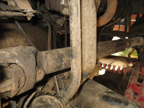 1987 Ford Bronco - A close-up view of the undercarriage of a vehicle, showing a heavily soiled driveshaft and universal joint assembly. The metal components a…