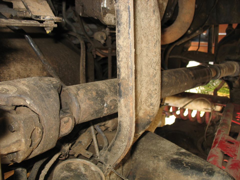 Undercarriage view of a dirty driveshaft and U-joint assembly on a vehicle.