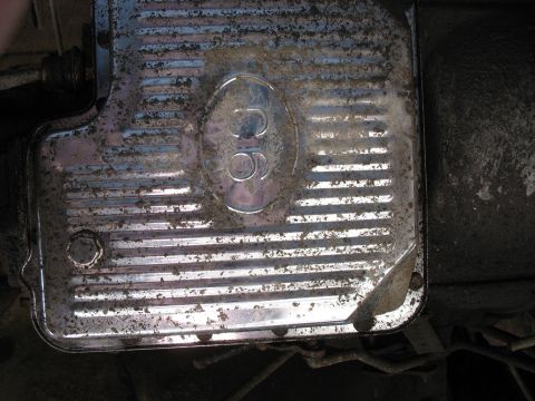 1987 Ford Bronco - A close-up, low-angle view of a dirty, chrome-plated transmission pan with horizontal ridges and a circular emblem featuring the number '30…
