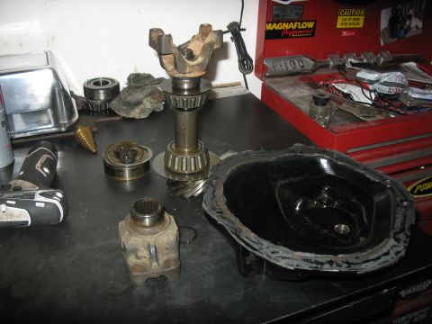 1987 Ford Bronco - A collection of automotive differential parts, including a ring gear, pinion, bearings, and a differential cover, are laid out on a workben…