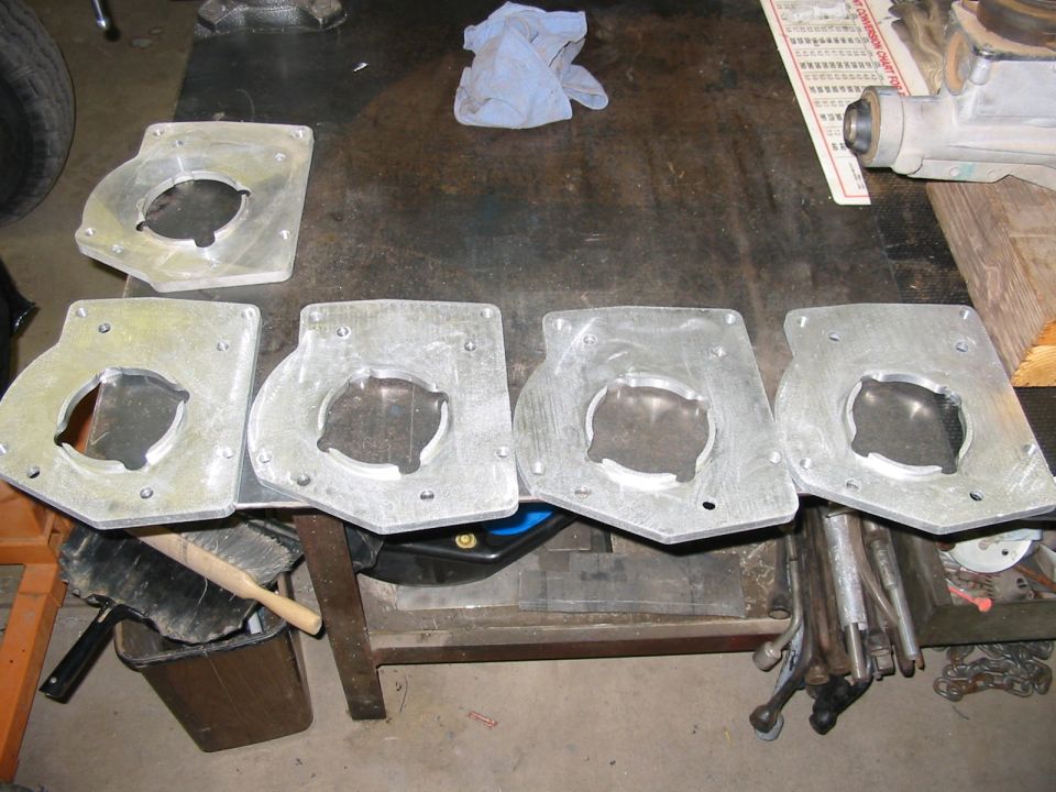 Four aluminum adapter plates with circular cutouts on a workbench.