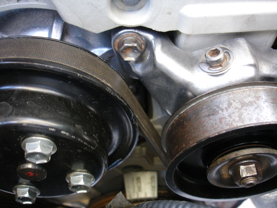 Close-up of accessory drive belt, black pulley, and rusty idler pulley on an engine