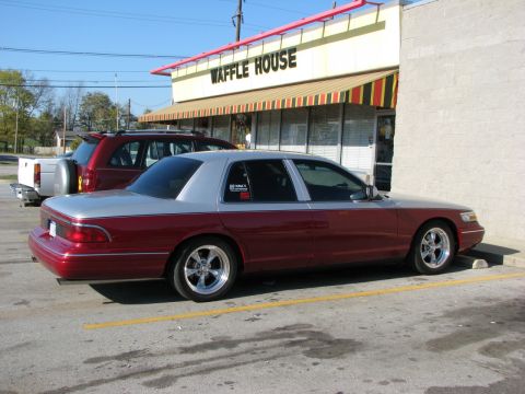 1993 Ford Crown Victoria - A two-tone maroon and silver Ford Crown Victoria is parked in front of a Waffle House. The sedan has custom chrome wheels and is angled tow…