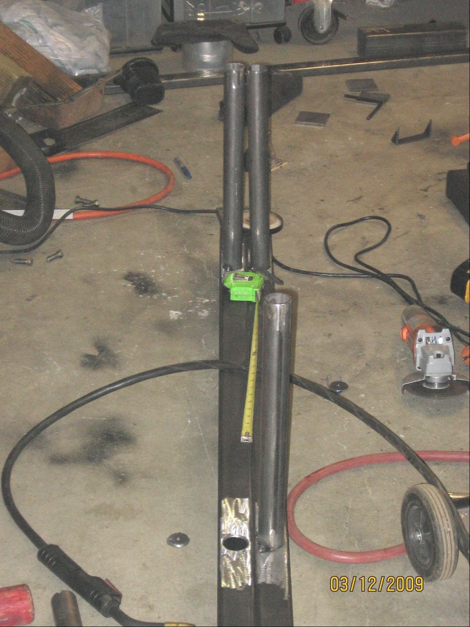 Metal tubing with a tape measure attached, surrounded by tools and workshop materials.