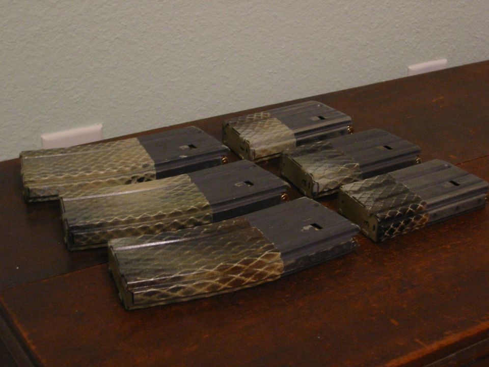 Seven rifle magazines with patterned wraps arranged on a wooden table.