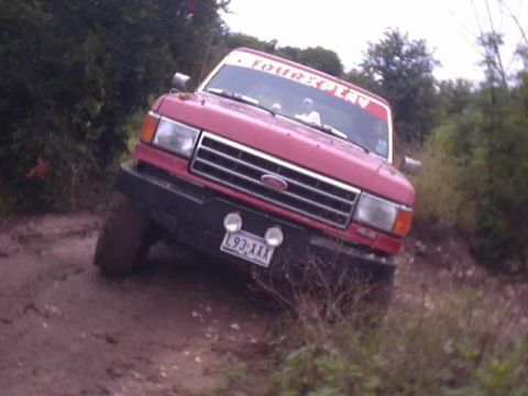 1989 Ford Bronco - This red Ford Bronco is navigating a muddy trail, with a festive sticker on its windshield.