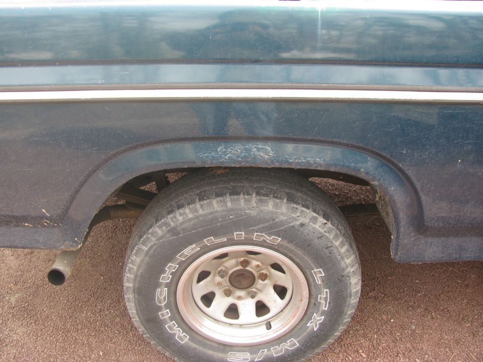 Dark blue pickup truck rear wheel well and exhaust pipe with Michelin tire.