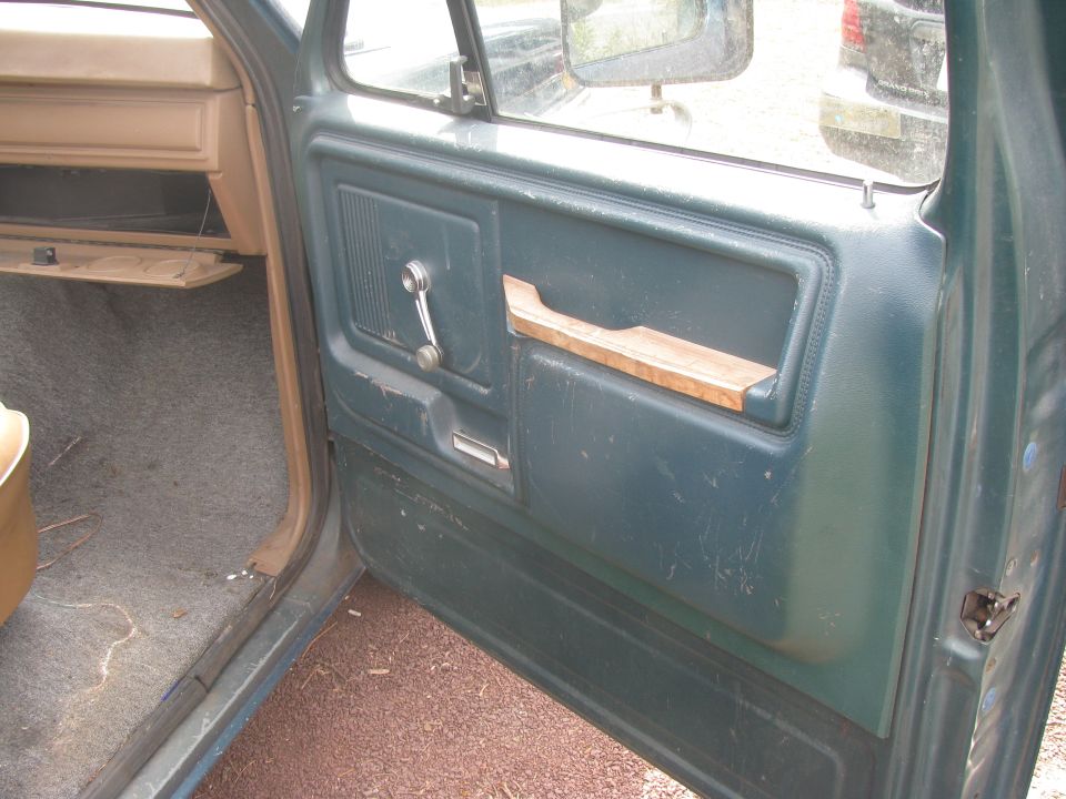 Interior of a dark green truck door, showing window crank, wooden pull, and lock.