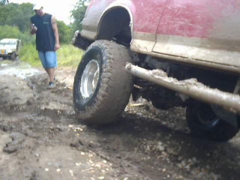 1989 Ford Bronco - A person stands next to a mud-covered vehicle navigating a difficult off-road path.