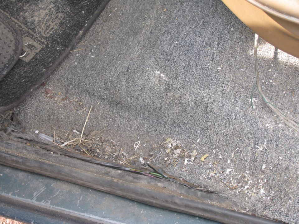 Dirty vehicle interior floor with debris and exposed wires.