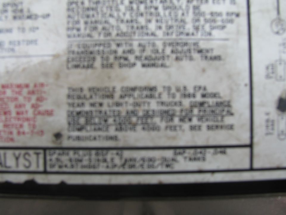 Blurred underhood emissions label with EPA compliance text and spark plug specification