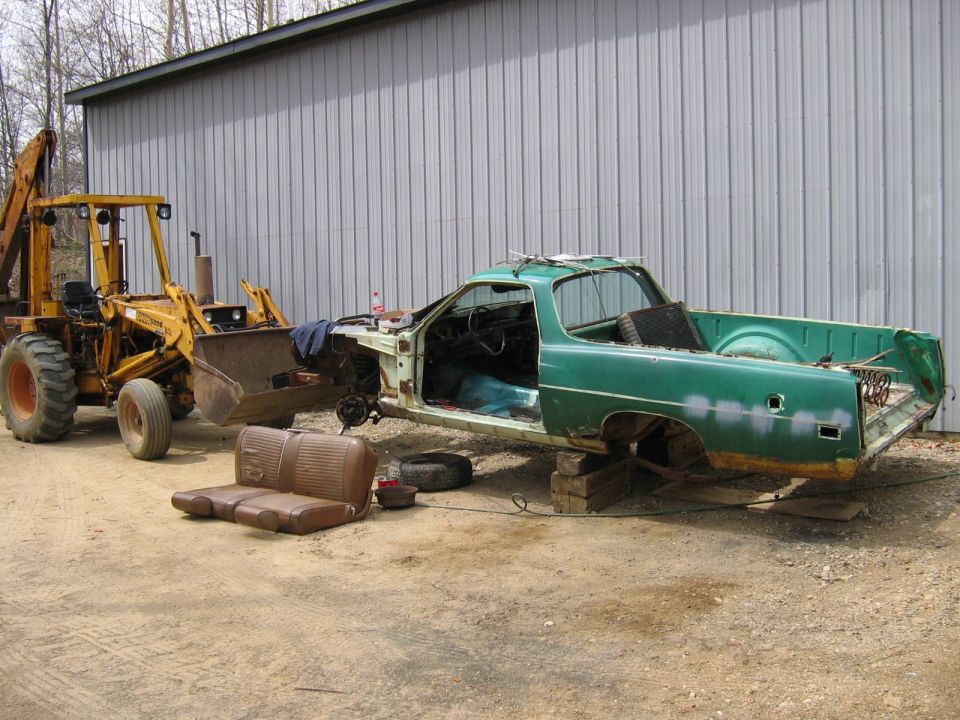 Green Ford Ranchero body with a yellow backhoe loader and a bench seat.
