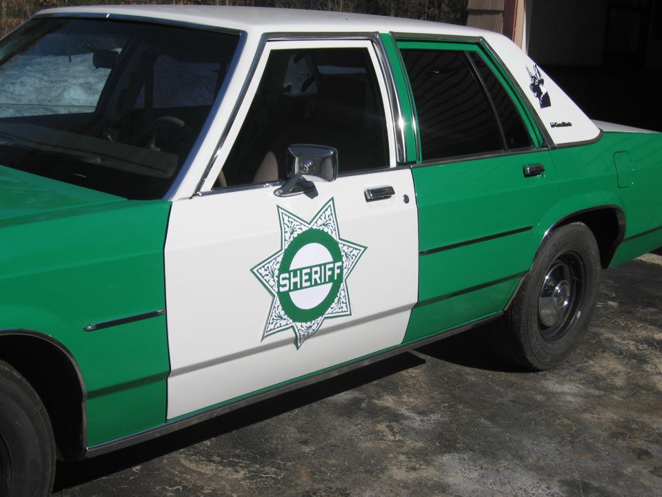Front door of a green and white Ford sedan with green Sheriff star badge