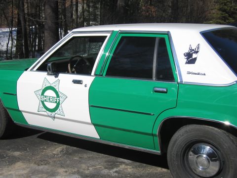 1991 Ford LTD Crown Victoria - Passenger-side view of the green-and-white Ford Sheriff sedan showing the green star badge and a German shepherd K-9 decal.