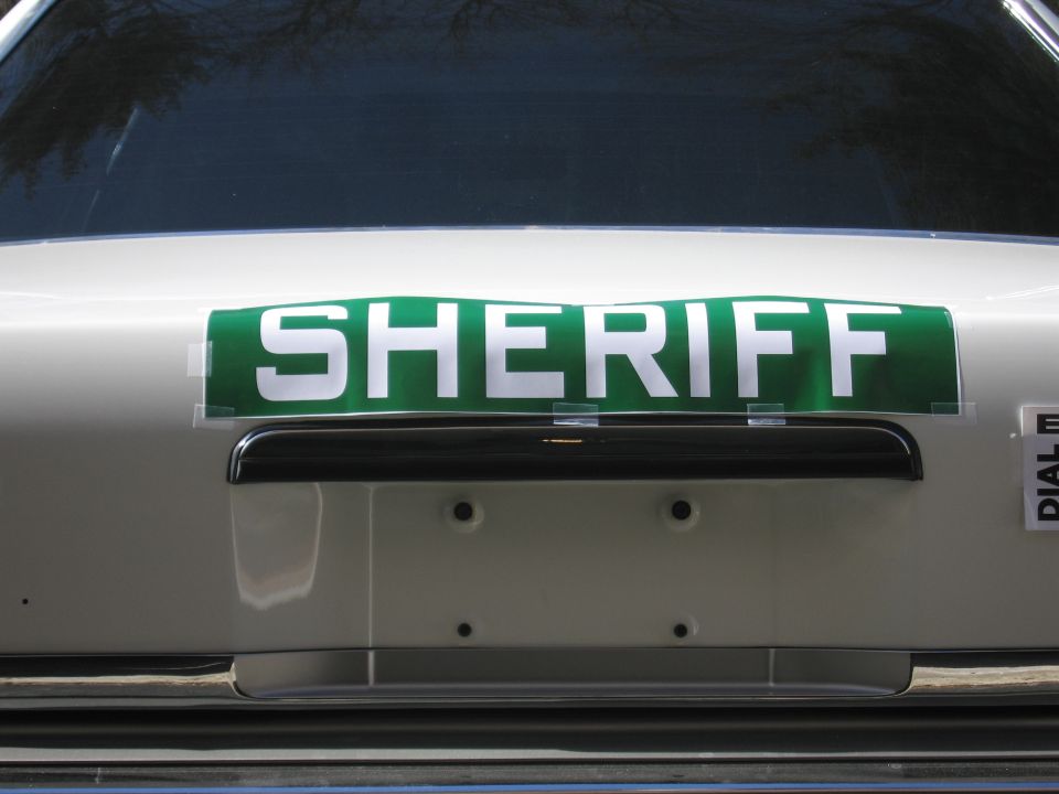 Close-up of green-and-white SHERIFF placard on the trunk of a sedan