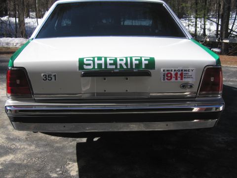 1991 Ford LTD Crown Victoria - Rear view of a white-and-green SHERIFF sedan with chrome bumper, 351 and DIAL 911 decals, photographed with snow patches behind.