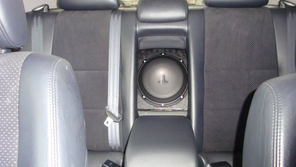 JL Audio subwoofer mounted in rear armrest pass-through of black leather and cloth back seat