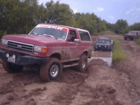 1989 Ford Bronco - Red 1989 Ford Bronco navigating an off-road trail with other vehicles present.