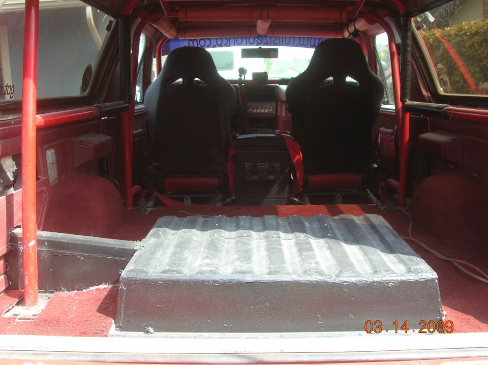 Interior of a red 1985 Ford Bronco with racing seats and rear storage box.