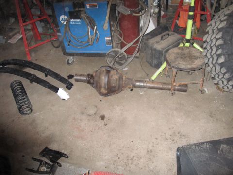 1992 Ford Bronco - Photograph of a vehicle axle and leaf spring laid out on a garage floor, not a document.