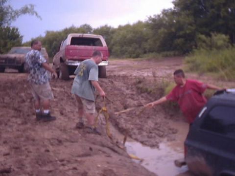 1989 Ford Bronco - People attempt to free a red SUV stuck in a muddy ditch.