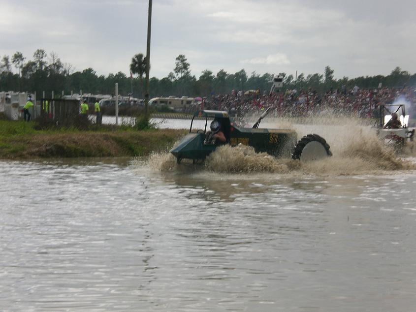 Green number 28 swamp buggy racing through muddy water with big spray