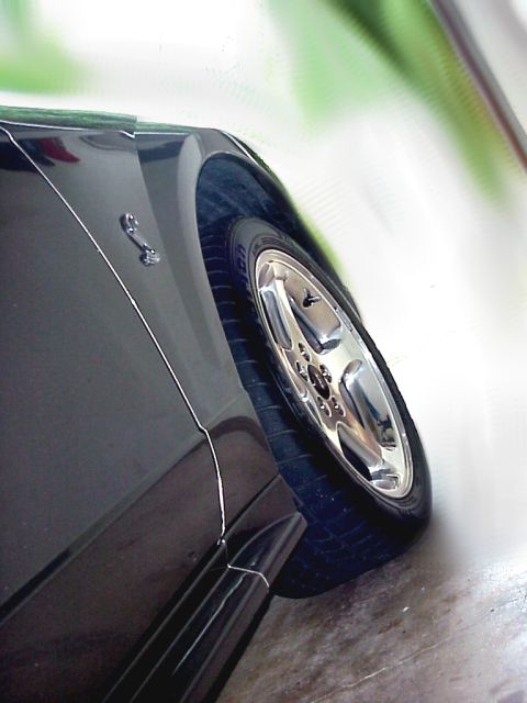 2001 Ford Mustang - Close-up of the fender and chrome wheel on a black 2001 Ford Mustang, the iconic pony emblem.