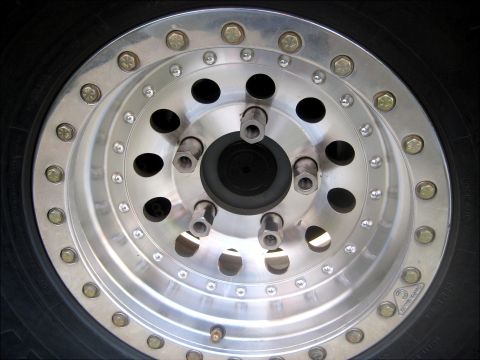 1996 Ford Bronco - A close-up shot of a polished aluminum wheel with multiple lug nuts and holes, mounted on a black tire.