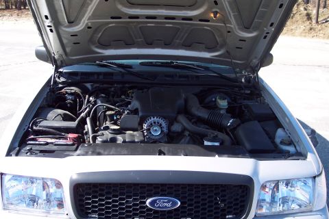 2001 Ford Crown Victoria - The open hood of a silver 2001 Ford Crown Victoria reveals the engine bay, including the battery, alternator, and air intake system.