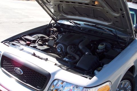 2001 Ford Crown Victoria - The open hood of a silver 2001 Ford Crown Victoria reveals its engine bay and the front grille with a Ford emblem. The engine compartment s…