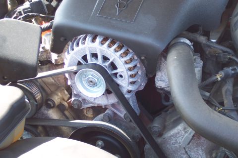 2001 Ford Crown Victoria - A close-up view of the alternator and serpentine belt system in a vehicle engine bay. The alternator housing is silver with visible copper…