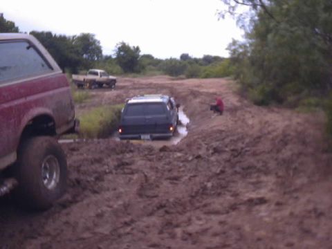 1989 Ford Bronco - Several vehicles navigate a muddy off-road trail with one SUV stuck in the mire.