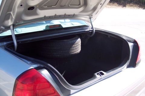 2001 Ford Crown Victoria - The open trunk of a silver sedan reveals a spare tire and the car's interior. The trunk lid is propped open by silver arms, and the car's t…