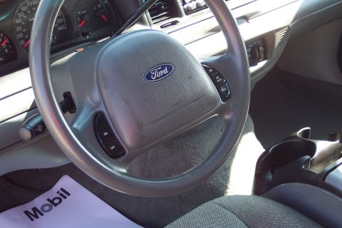 2001 Ford Crown Victoria - Interior view of a Ford Crown Victoria steering wheel and dashboard, featuring the Ford logo on the airbag cover and cruise control buttons…