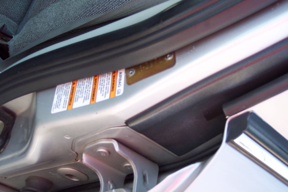 Close-up of a vehicle door jamb with an airbag warning sticker and a metal plate.