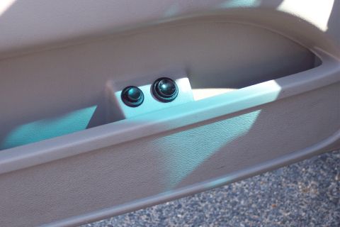 2001 Ford Crown Victoria - A close-up view of two black buttons on a tan interior car door panel. The buttons are located within a recessed storage area, and sunlight…