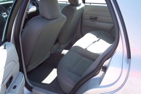 2001 Ford Crown Victoria - The interior of a silver sedan shows the rear passenger seats and door panel. Sunlight streams in, highlighting the textured fabric of the…
