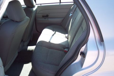 2001 Ford Crown Victoria - The interior of a car shows the rear passenger seats and door panel. Sunlight streams across the fabric seats and gray carpeted floor.