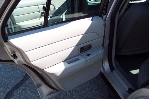 2001 Ford Crown Victoria - The interior of a car shows the driver's side rear door panel and the edge of the front passenger seat. The door panel is light gray with h…