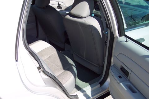 2001 Ford Crown Victoria - The interior of a white 2001 Ford Crown Victoria is shown, focusing on the rear passenger seats and door panel. The seats are grey cloth wi…